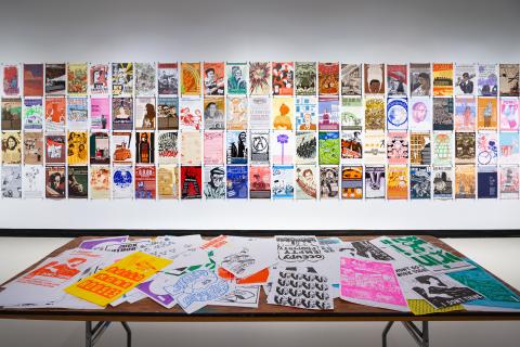 Colorful image of gallery wall of posters with table covered in materials in front of it