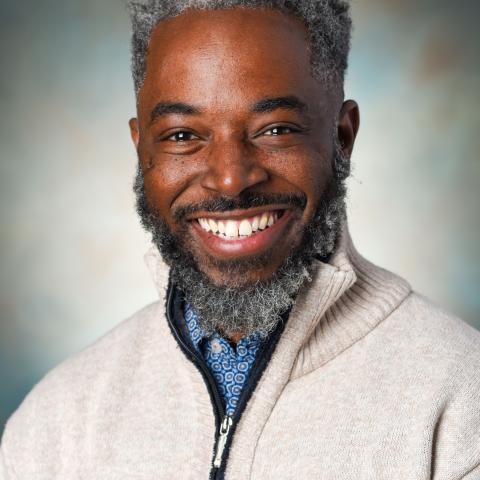 Color image of smiling African American man with beard and mustache wearing a zip front cardigan