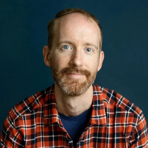 White man with facial hair wearing a plaid shirt