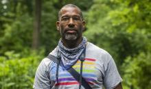 Image of African American Man outside in front of trees wearing a tee-shirt and bandana