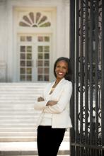 Image of smiling African American woman leaning against a black gate in front of an ornate white building
