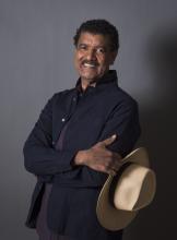 Image of smiling man with mustache wearing a blue shirt and holding a hat