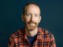 White man with facial hair wearing a plaid shirt