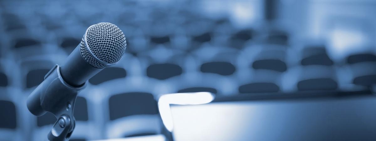 Close up image of a microphone on a podium with empty rows of seats in the background