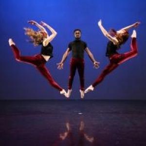 Three dancers jumping towards the middle of the photo.