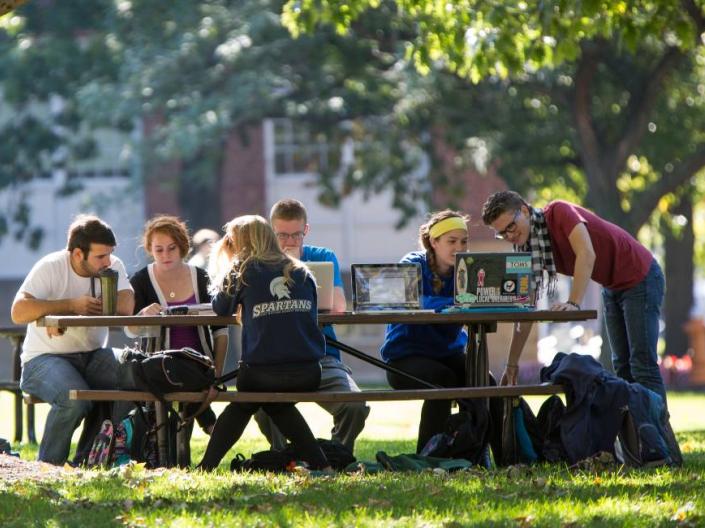 CWRU students sitting outside on benches under a tree