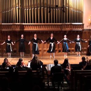 A group of baroque dancers perform on stage with an orchestra playing in the pit