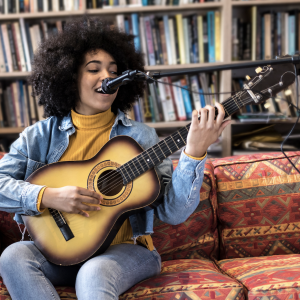 Haven Hour Cover Photo: female playing guitar, singing, sitting on red sofa