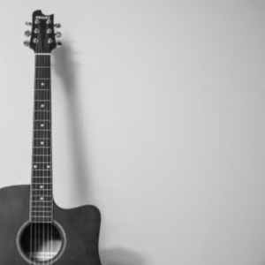 A black and white image of an acoustic guitar leaning against a wall