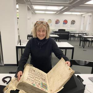 A middle-aged woman opens a large, centuries-old tome