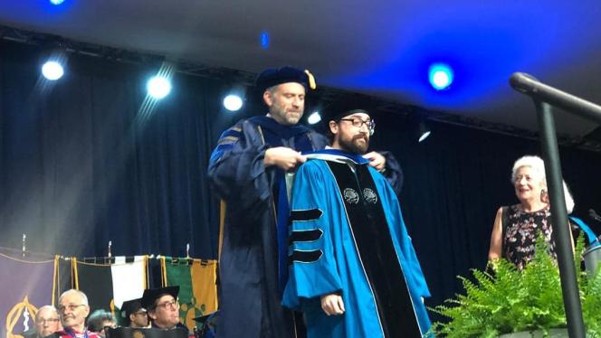 Dr. Daniel Goldmark placing academic hood over male student.