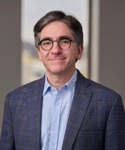 A smiling man in a crisp blue suit and glasses