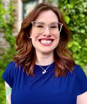 Jessica L. Gallagher-Steuver - smiling brunette woman in a blue top standing in front of a green background