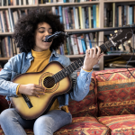 Haven Hour Cover Photo: female playing guitar, singing, sitting on red sofa