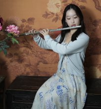 Erin Huang, young female student with dark hair wearing dress with blue flowers, playing flute.