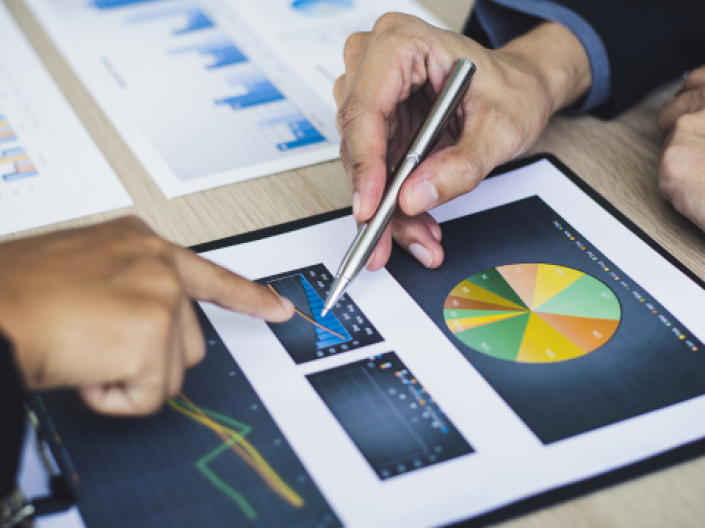 The image features a pair of coworkers who review bar and pie charts during a meeting. 