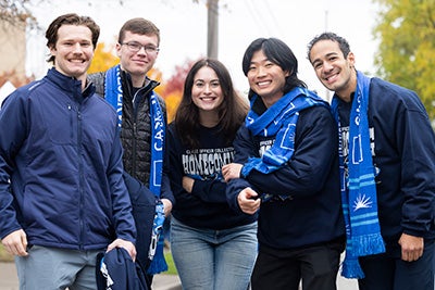 Five people smiling outdoors with blue scarves