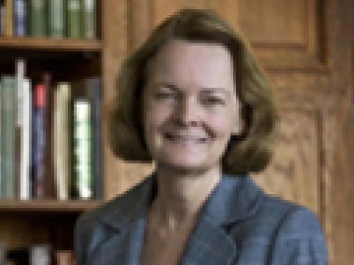 Kathleen Wells smiles at camera in front of bookshelf while wearing formal attire
