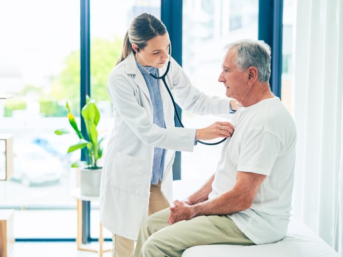 Image of a white female doctor using a stethoscope on a white male elderly patient