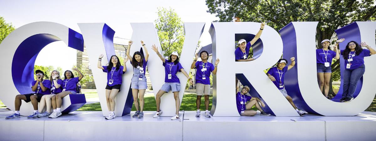 Students in CWRU shirts pose with the CWRU letters by Adelbert Hall.