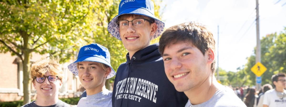 Four students pose for a photo wearing CWRU-branded shirts, sweatshirts, hoodies, and hats.