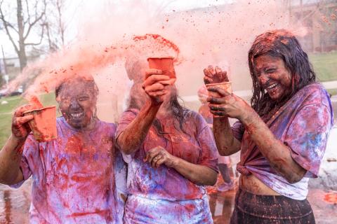 Three students participate in Holi, covered in red and blue dust.