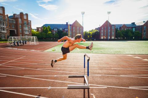 An athlete jumps over a hurdle on the outdoor track.