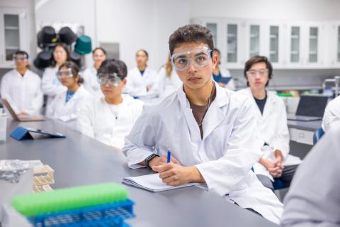 Students in a labratory setting wear PPE while taking notes.