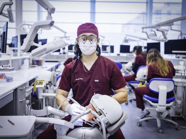 A dental student looking towards the camera as they prepare to work on a dental dummy.