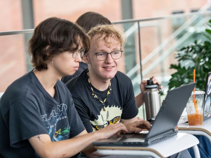Two students sit at a dark and work together on a laptop.