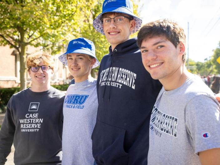 Four students pose for a photo wearing CWRU-branded shirts, sweatshirts, hoodies, and hats.