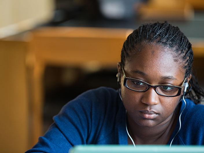 Female student with earbuds looking at computer.