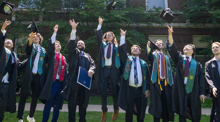 Graduates jumping and throwing graduation caps in the air.