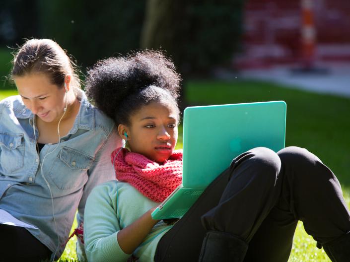 Two girls sitting on the grass with a laptop.
