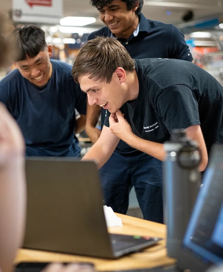 Three students smiling while looking at a laptop together