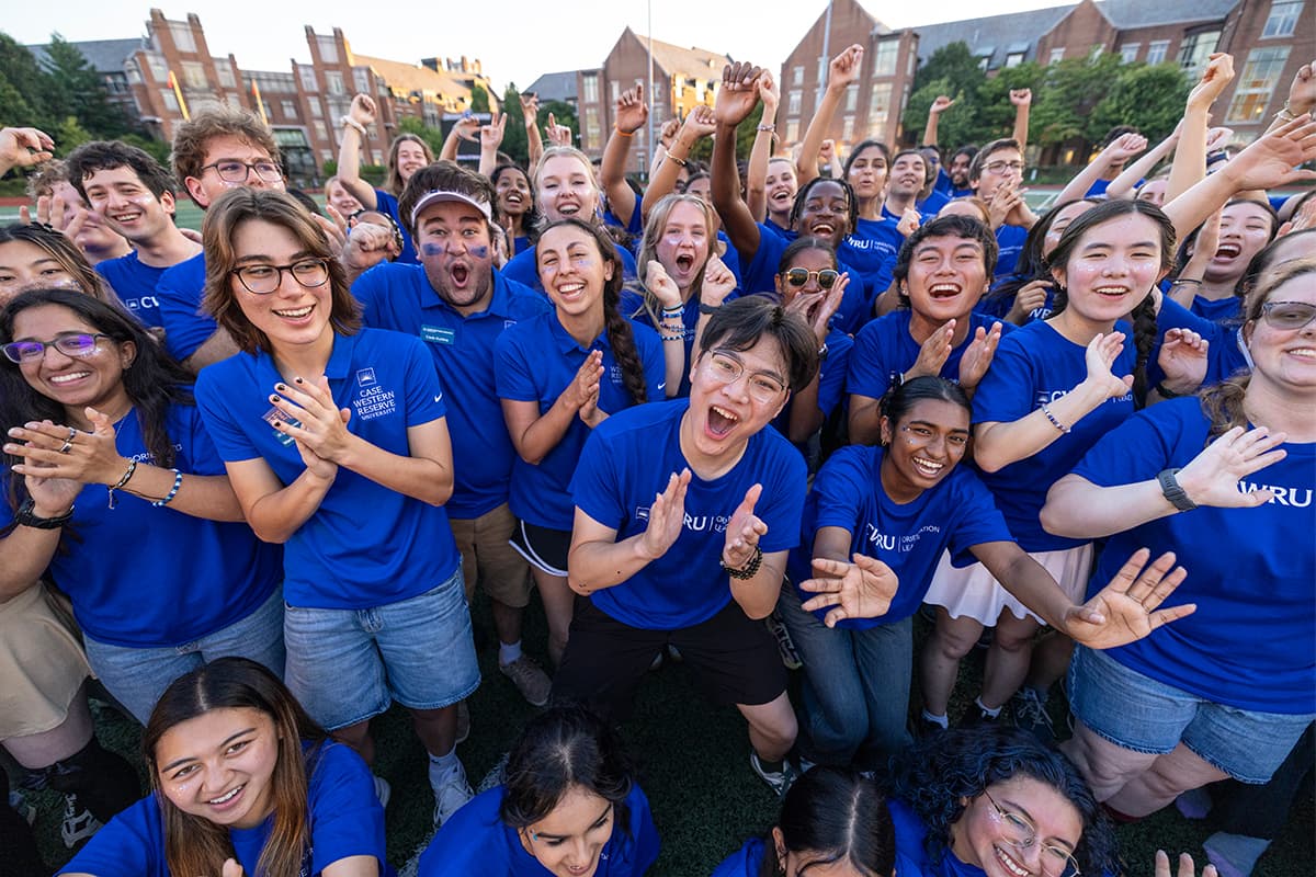 A large group of Case Western Reserve University students in blue shirts cheering together on campus