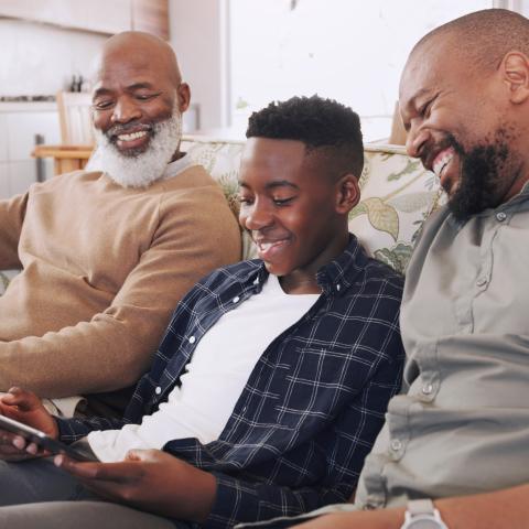 Three generations of African American males sitting on couch smiling. 