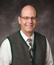 Image of Steven E. Waggoner wearing sweater vest and white dress shirt, tie and glasses. 