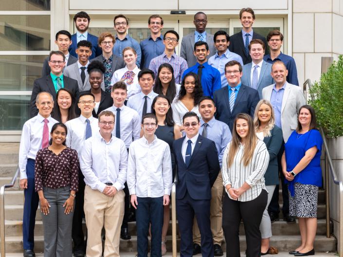 Students gathered for a group photo on the stairs of the Wolstein Research Building with program staff and Director Stan Gerson, all smiling.