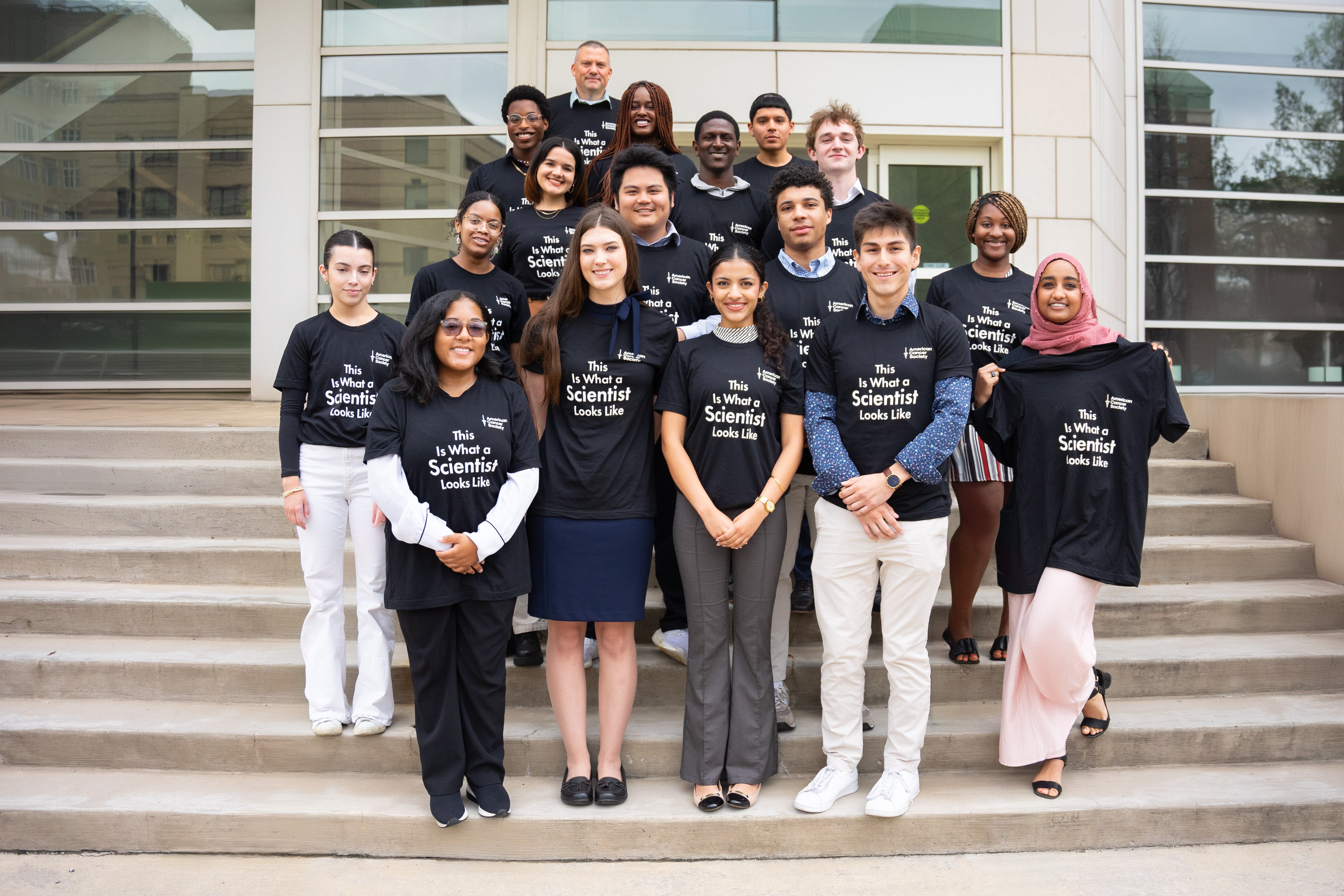 ACS supported cancer research students wearing "This is what a scientist looks like" t-shirts while posing on the steps outside the Wolstein Research Building