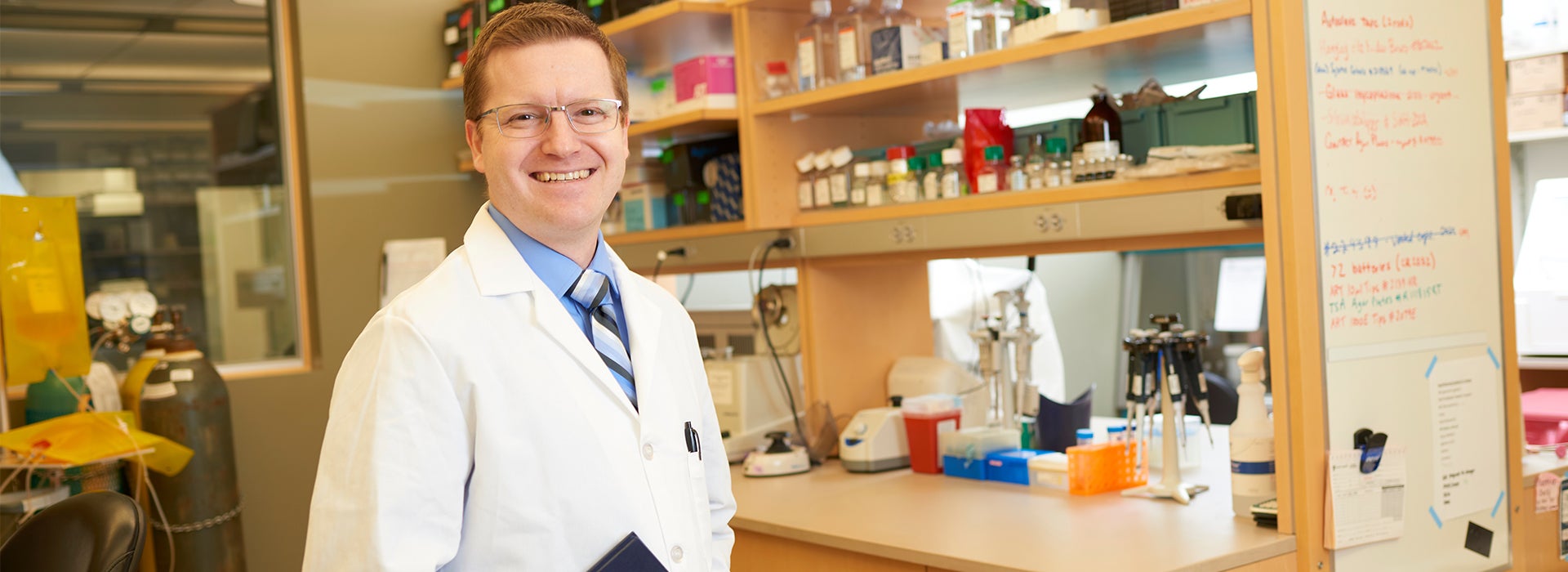 Cancer researcher standing in a biomedical research laboratory surrounded by scientific equipment and laboratory supplies