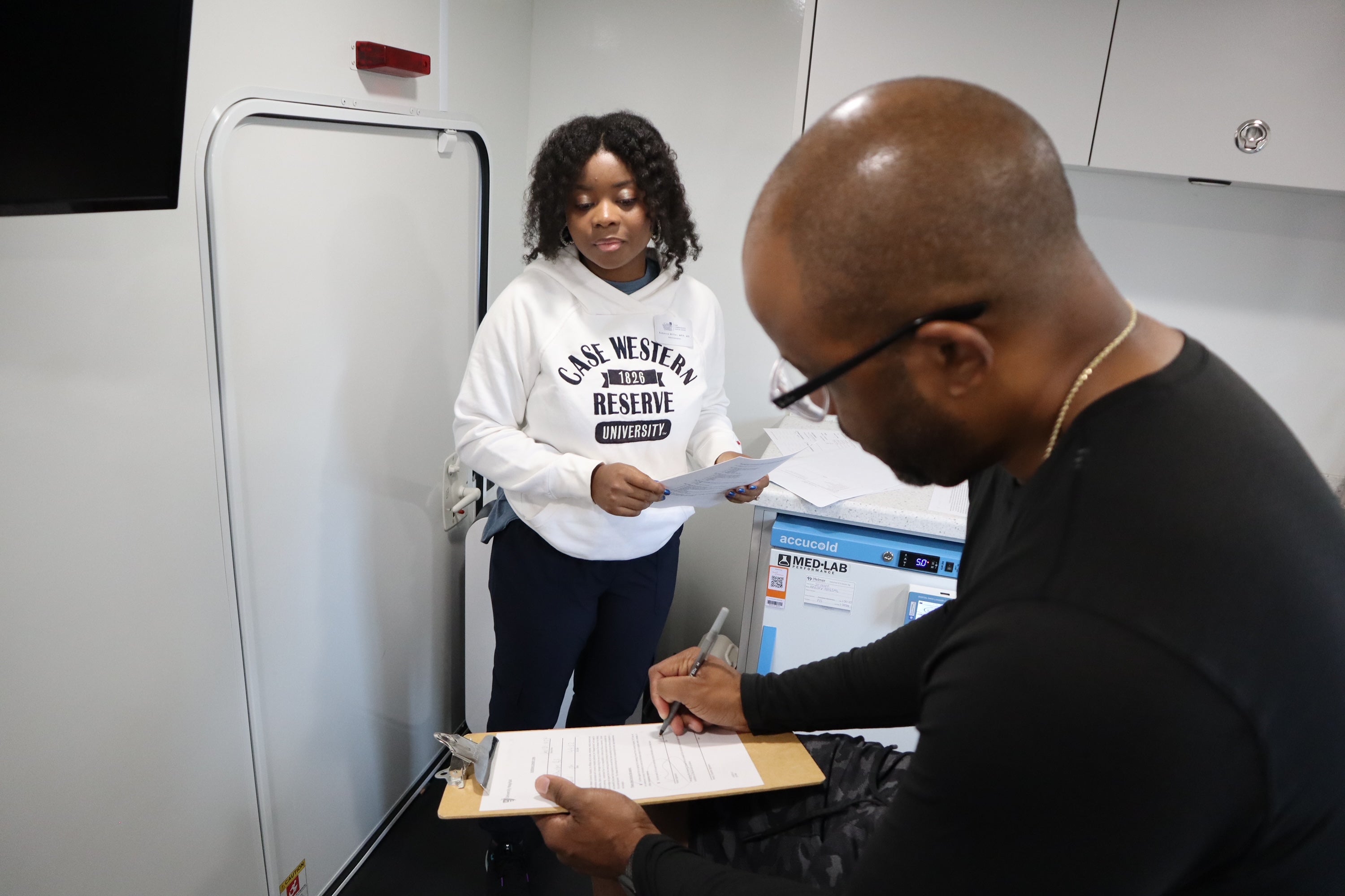 Individual completes paperwork with assistance from a staff member in a clinical setting.