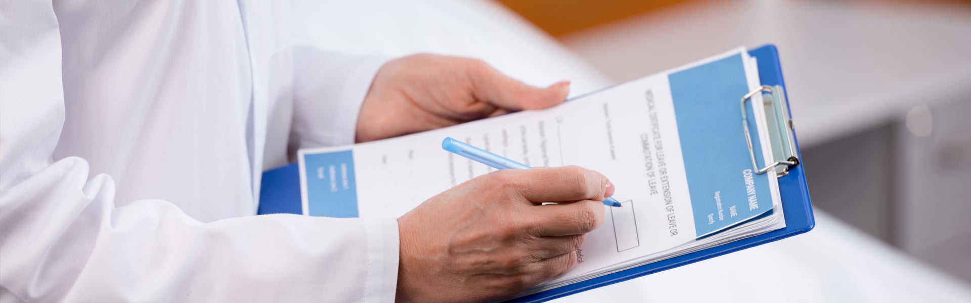 Healthcare professional filling out forms on a clipboard in a clinical setting.