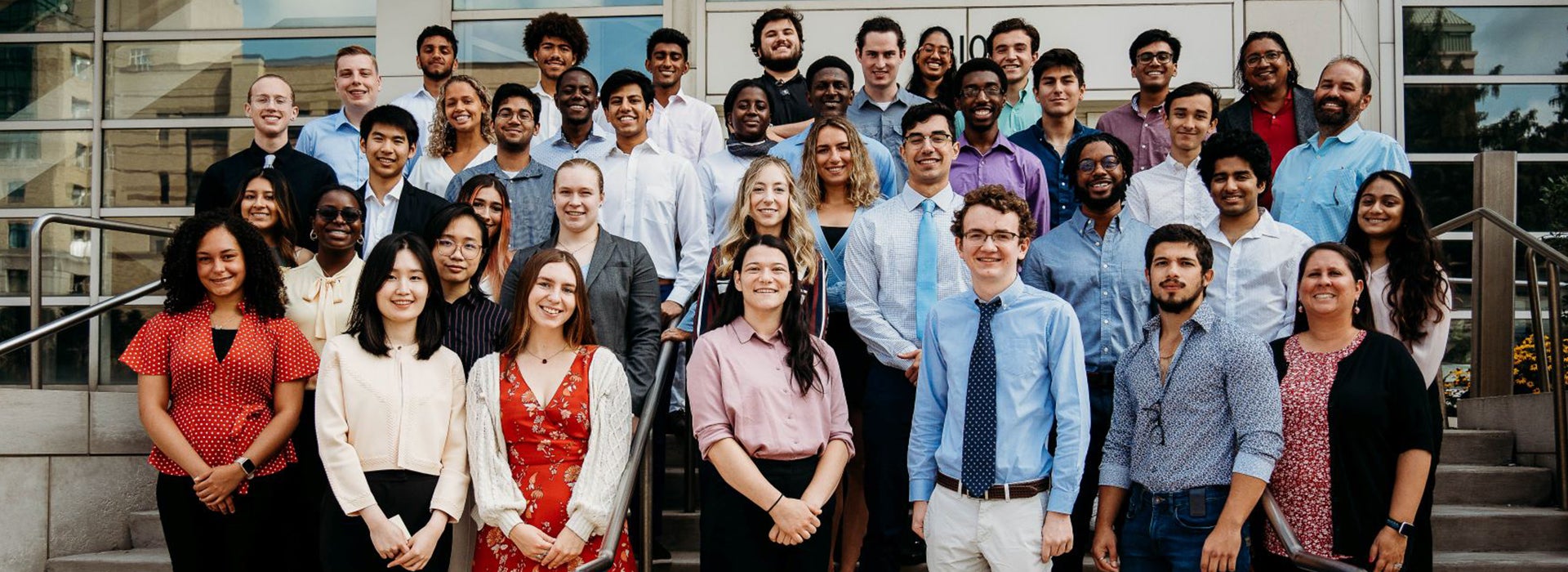 Diverse group of students and staff standing together on outdoor steps in front of a university building for a group portrait.