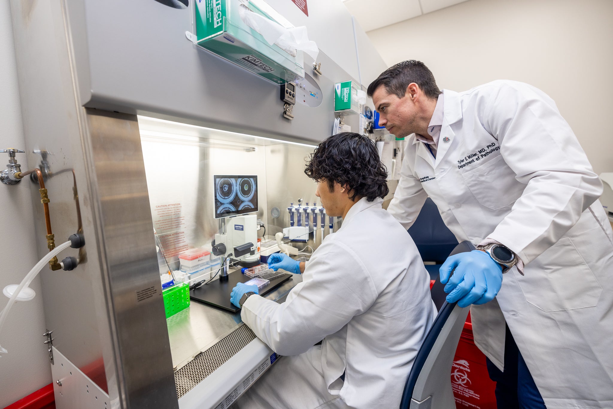 Two researchers in laboratory coats examine samples and data together while working at a laboratory bench.