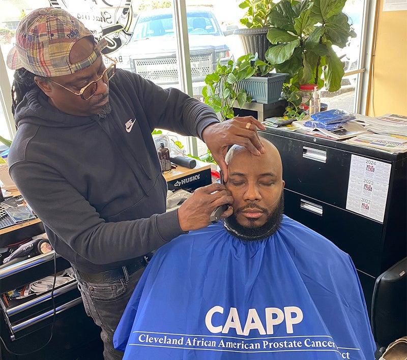 A barber tends to a client sitting in a chair
