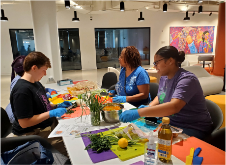 Three people wearing blue gloves prepare fresh vegetables together at a table during a hands-on healthy cooking activity.