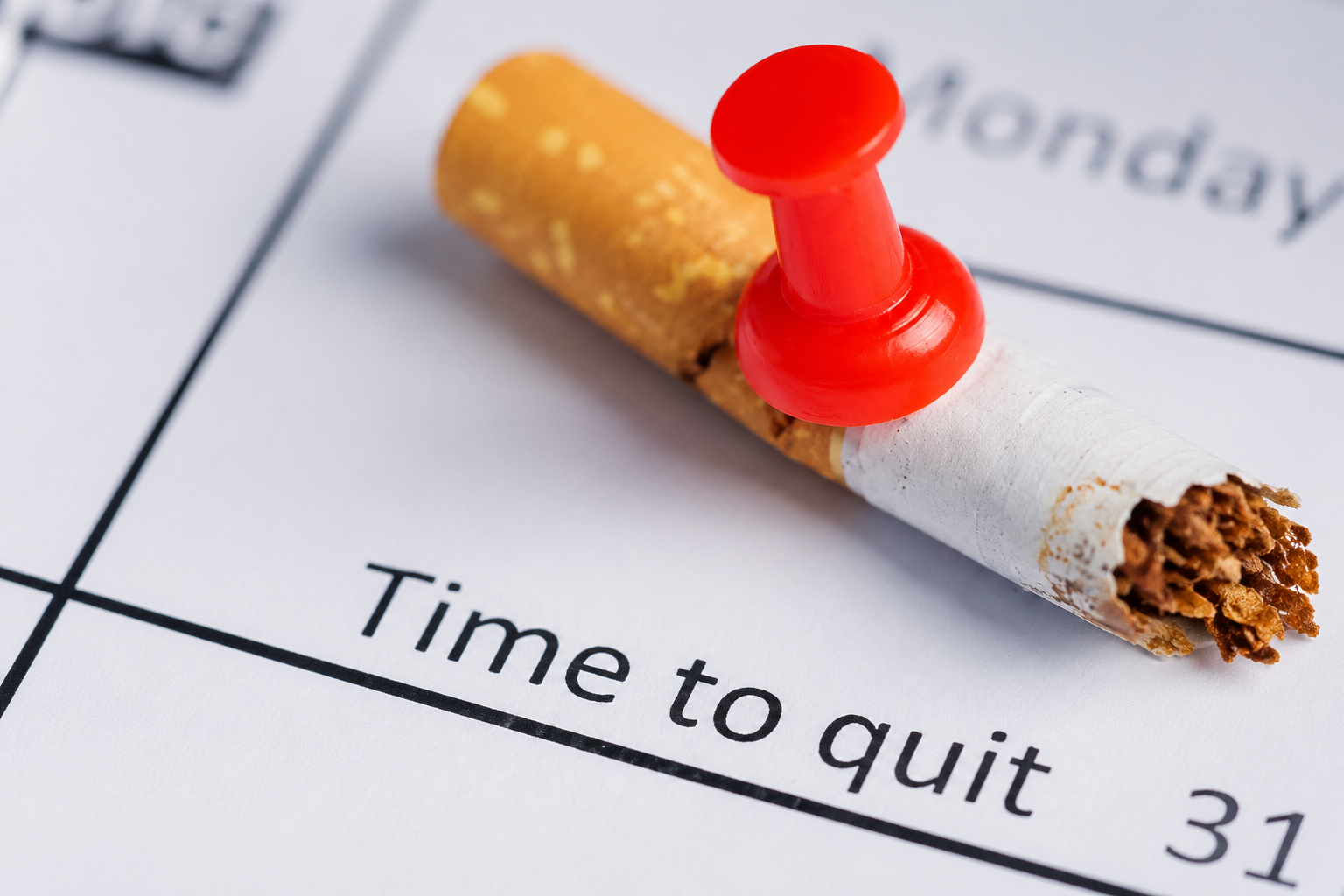Broken cigarette pinned to a calendar with a red pushpin above the words “Time to quit.”