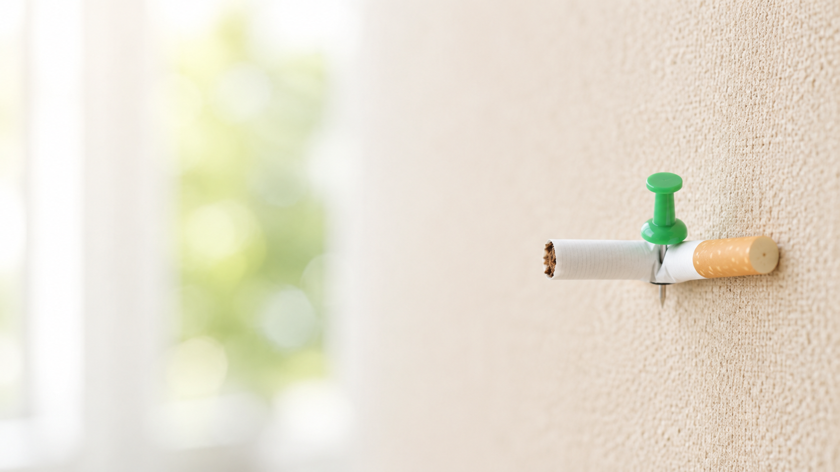 Cigarette pinned to a wall with a pushpin, symbolizing quitting smoking.