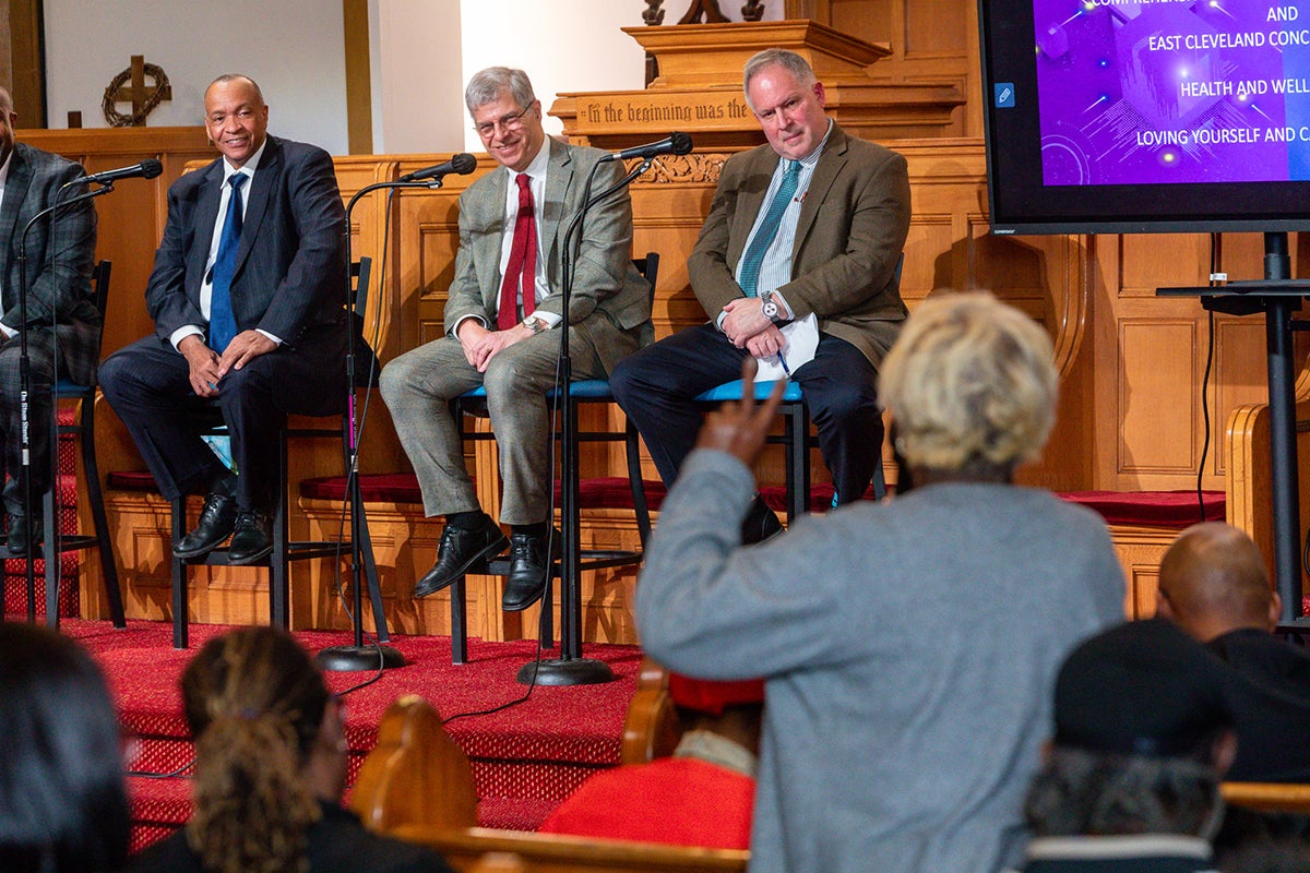 Audience member raises a hand during a panel discussion with three speakers seated on stage in a church auditorium.